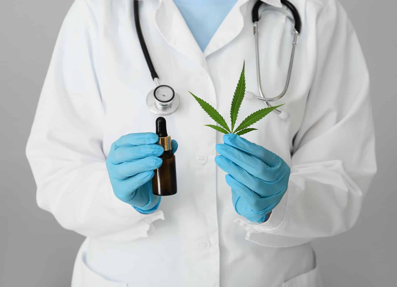 Laboratory worker with bottle of hemp oil on grey background, closeup
