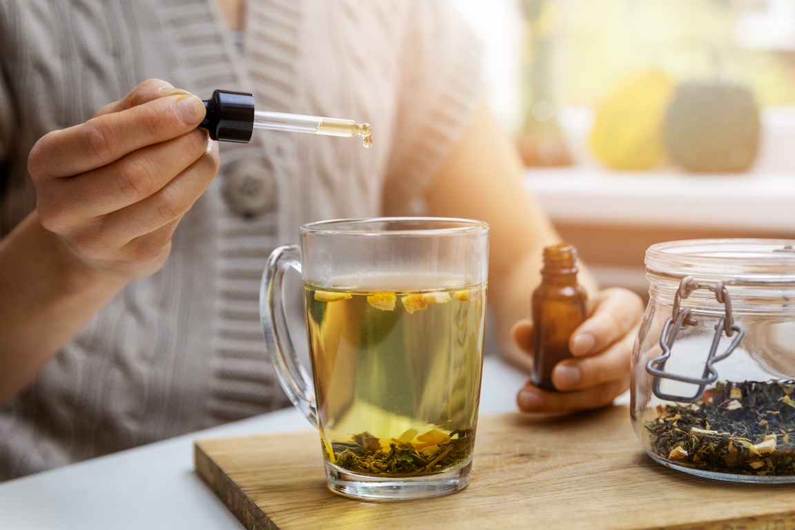 dietary supplements and vitamins - woman adding drop of cbd oil in cup of tea with pipette. anti stress