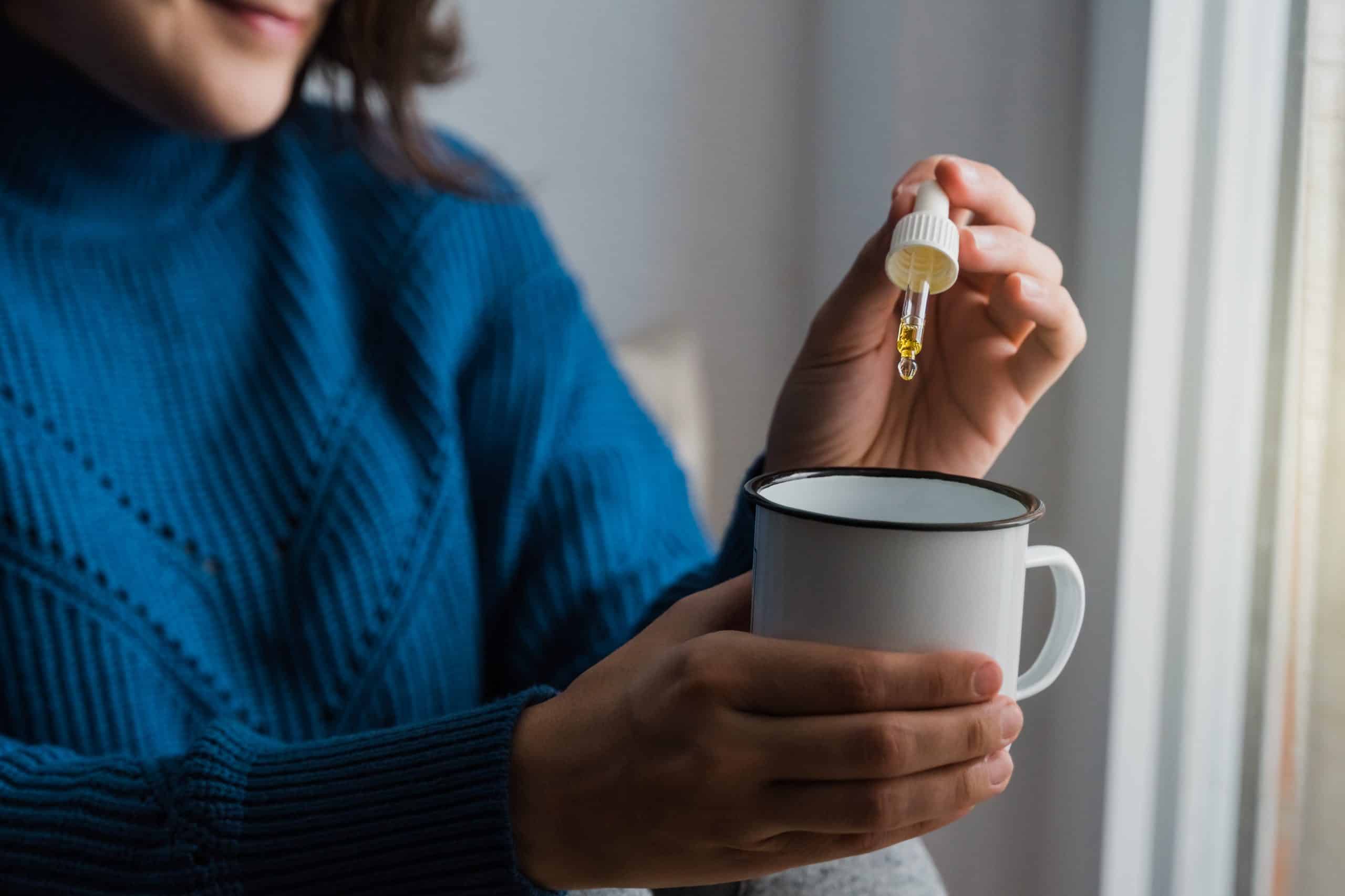 Woman taking Cannabis cbd oil inside tea cup - Alternative medicine, vitamins and supplements concept - Focus on dropper